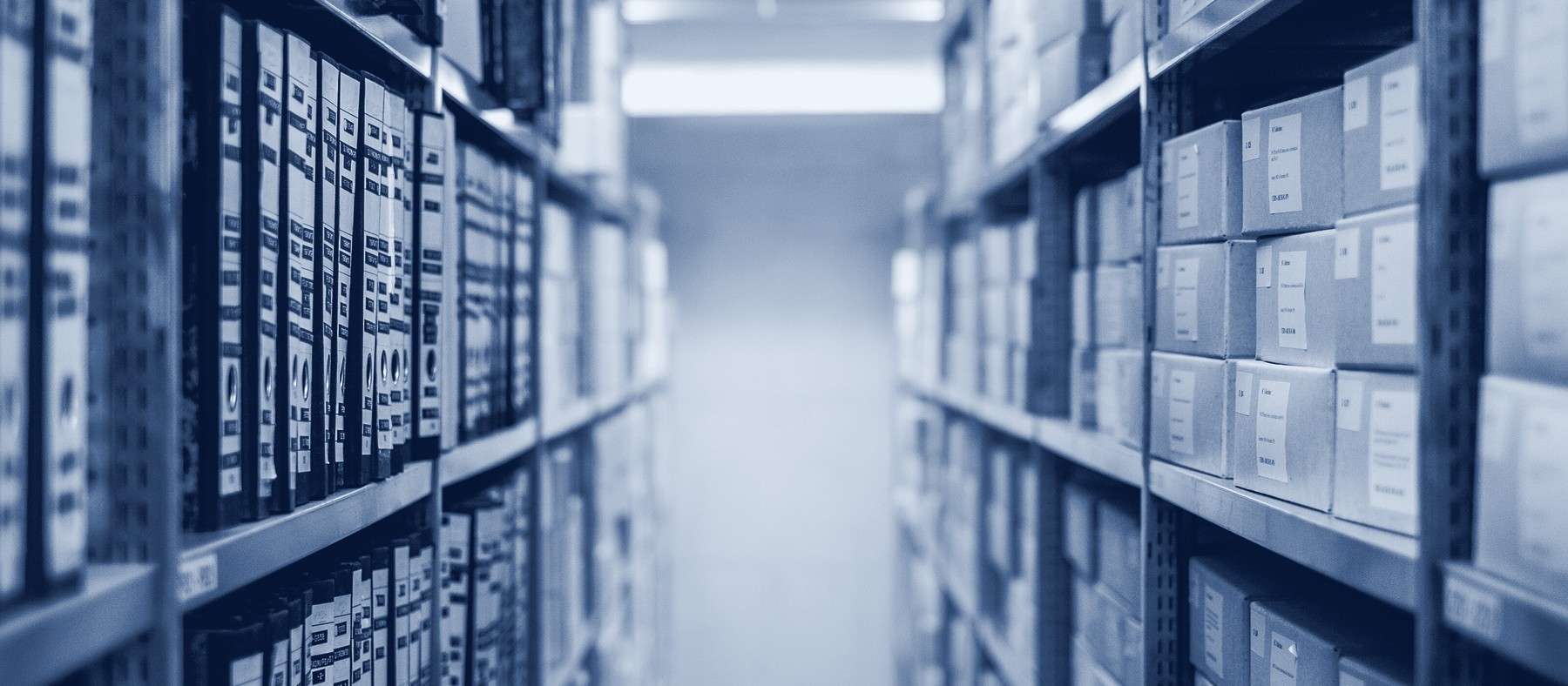 A narrow aisle between tall archive shelves filled with binders and storage boxes.