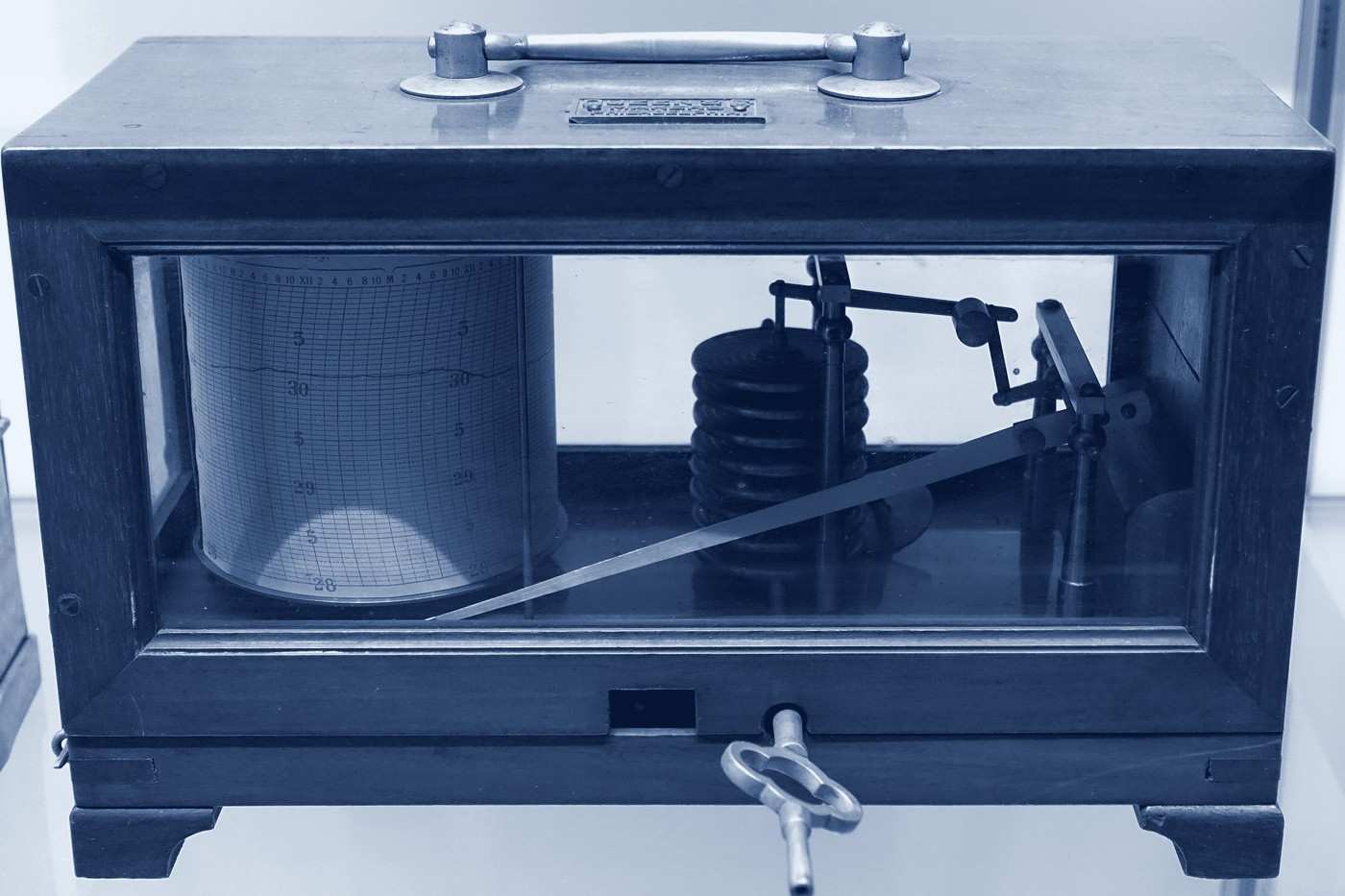 A barograph in a glass-sided wooden case, its pen resting on a ruled paper drum.