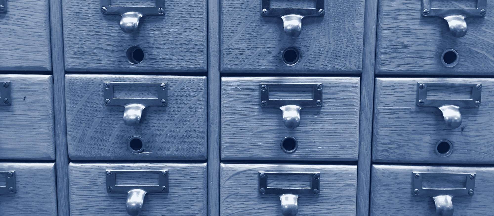 Rows of small oak card-catalogue drawers, each with a brass pull and label holder.