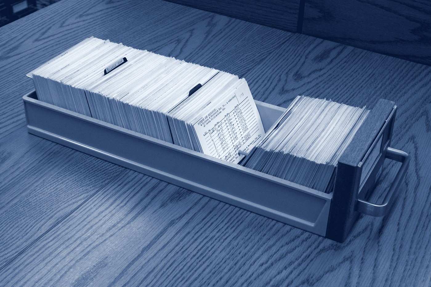 A long metal card-catalogue drawer pulled out onto a wooden table, packed with typed index cards.