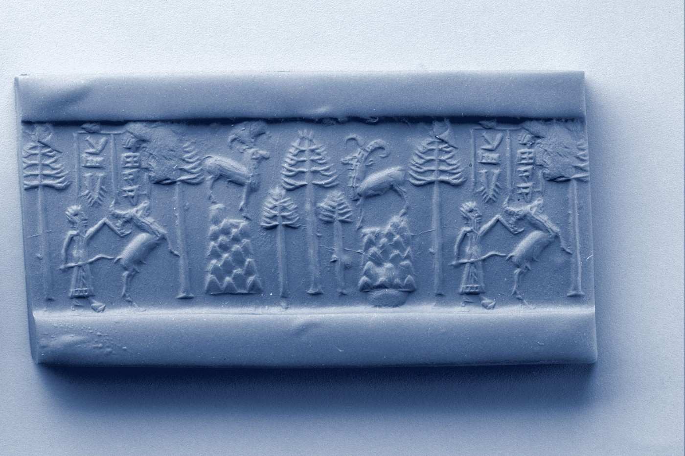 An Akkadian stone cylinder seal beside the long impression it leaves when rolled across clay.