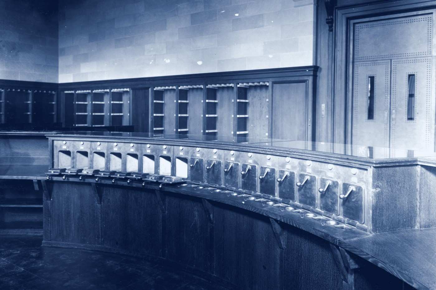 A curved control desk lined with pneumatic tube stations in an archive reading room.