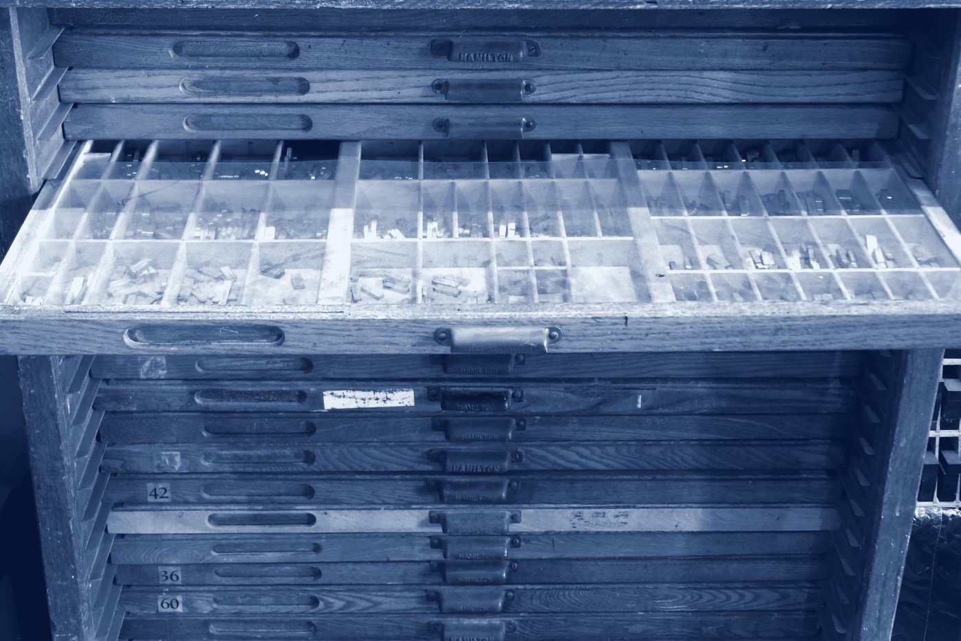 An open printer’s type-case drawer divided into small compartments, with closed drawers below.